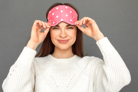 Freestyle. Young girl in sleeping mask standing isolated on grey smiling cheerful close-upの写真素材