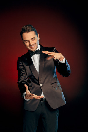 Professional Occupation. Showman in suit standing isolated on wall showing trick playfulの写真素材