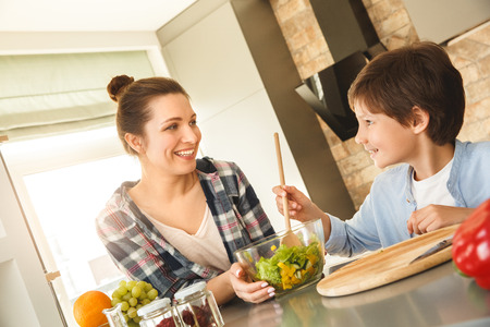 Family at home standing in kitchen together looking at each other happy son mixing saladの写真素材