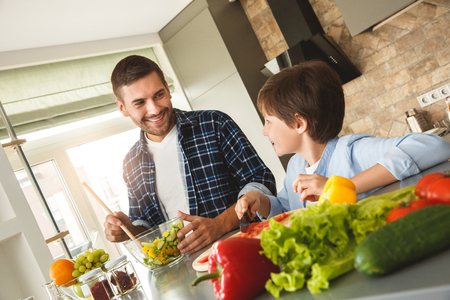 Family at home standing in kitchen making salad together talking smiling cheerfulの写真素材