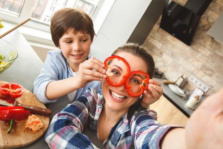 Family at home standing in kitchen together taking selfie photos son holding bell pepper on moms eyes smiling happy close-upの写真素材