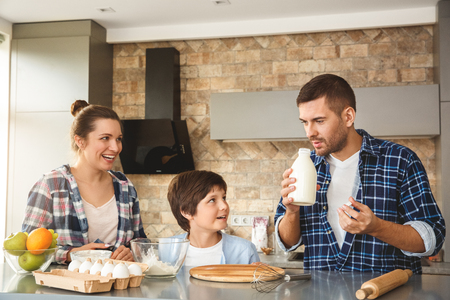 Family at home standing near table in kitchen making dough together father smelling milk thoughtfulの写真素材