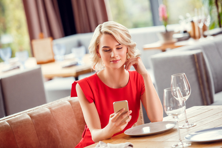 Young woman dining in restaurant sitting browsing smartphone joyfulの写真素材