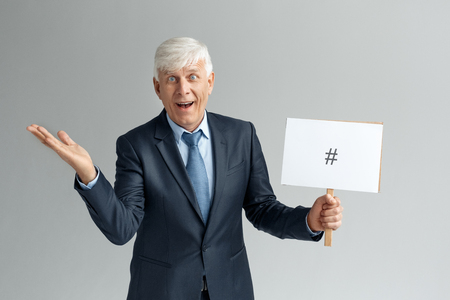 Business Lifestyle. Businessman standing isolated on gray holding board with pound sign smiling excitedの写真素材