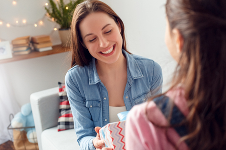 Mother and daughter at home mothers day sitting mother holding present box from daughter cheerful close-upの写真素材
