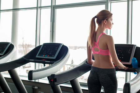 Young girl in gym healthy lifestyle walking on treadmill thoughtful back viewの写真素材
