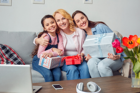 Grandmother mother and daughter together at home celebration sitting with presents hugging smilingの写真素材