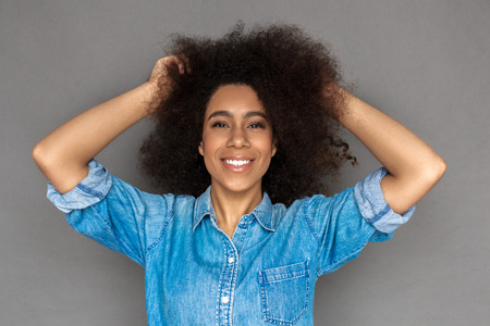 Freestyle. Mulatto woman standing isolated on grey touching hair laughing cheerful close-upの写真素材