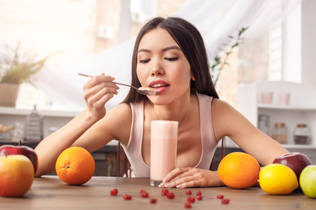 Young girl at kitchen healthy lifestyle sitting eating smoothie looking at spoon foretastingの写真素材