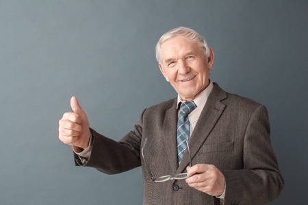 Senior man studio standing isolated on gray holding glasses showing thumb up positiveの写真素材