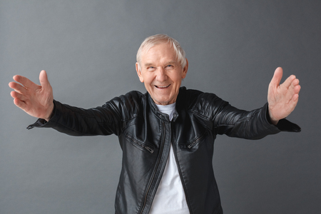 Senior man in leather jacket standing isolated on gray opening hands looking camera friendly close-upの写真素材