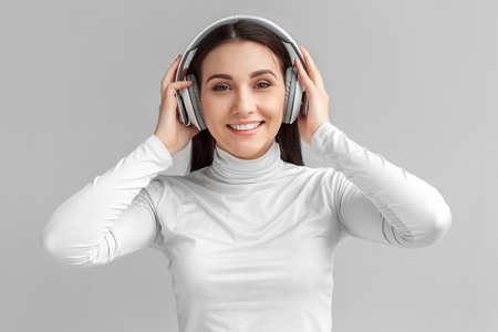 Freestyle. Woman in headset standing isolated on gray listening music looking camera happyの写真素材