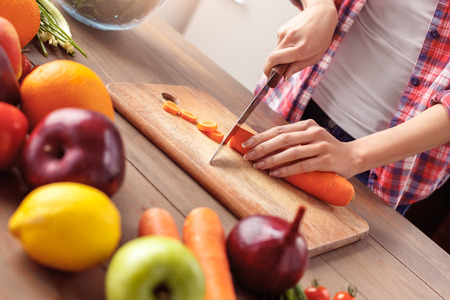 Young girl at kitchen healthy lifestyle standing cutting carrot preparing ingredients close-upの写真素材