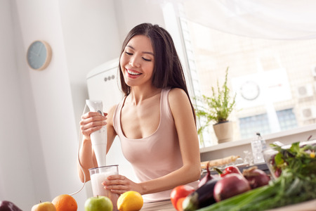 Young girl at kitchen healthy lifestyle standing making fruit yogurt with hand blender joyfulの写真素材