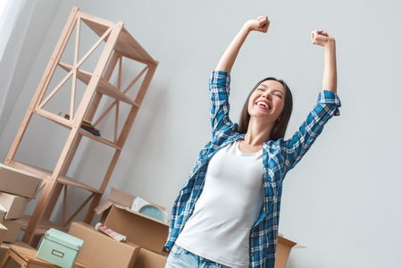 Young woman moving to a new place standing hands up happy bottom viewの写真素材