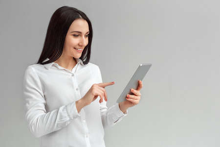 Freestyle. Woman standing isolated on gray browsing internet on digital tablet joyfulの写真素材
