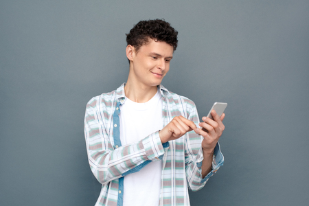 Man isolated on gray wall free style standing browsing internet on smartphone joyfulの写真素材