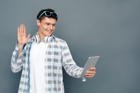 Man wearing headphones isolated on gray wall tourism concept standing talking with friend by video chat cheerfulの写真素材