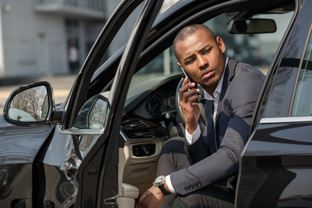 Young businessman sitting in car door opened talking on smartphone waiting for customerの写真素材