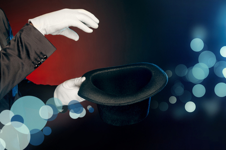 Professional Occupation. Showman in suit and gloves standing isolated on wall making tricks with hat close-upの写真素材