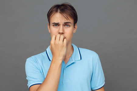 Bad habit. Teenager boy standing isolated on grey biting nails nervous close-upの写真素材