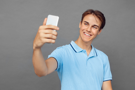 Freestyle. Teenager boy standing isolated on grey taking selfie on smartphone cheerful close-upの写真素材