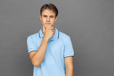 Creative thinking. Teenager boy standing isolated on grey touching chin thoughtfulの写真素材