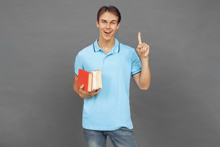 Freestyle. Teenager boy standing isolated on grey with books pointing up idea happyの写真素材