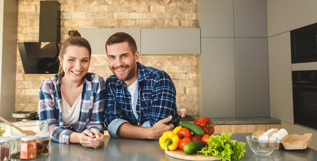 Young couple at home leaning on table in kitchen together looking cheerfulの写真素材