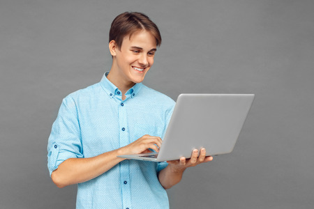 Freestyle. Teenager boy standing isolated on grey browsing laptop happyの写真素材