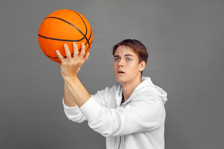 Freestyle. Teenager boy standing isolated on grey throwing ball concentrated close-upの写真素材