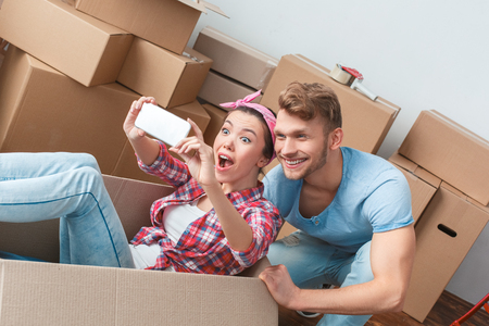 Young couple moving to new place woman in box taking selfie photos with man excitedの写真素材