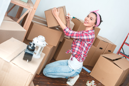 Young girl moving to new place standing on knees writing on box with marker smiling joyfulの写真素材