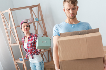 Young couple moving to new place woman standing passing casket to man carrying box concernedの写真素材