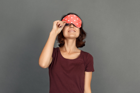 Freestyle. Young woman in sleeping mask isolated on grey looking camera playfulの写真素材