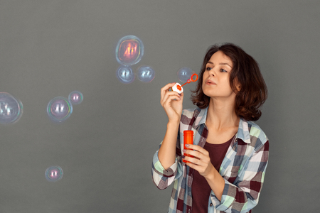 Freestyle. Young woman isolated on grey blowing bubbles concentratedの写真素材