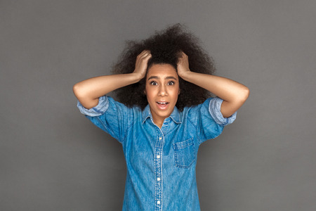 Freestyle. Mulatto woman standing isolated on grey holding hair looking camera surprisedの写真素材