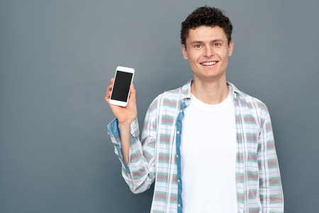 Man isolated on gray wall free style standing holding smartphone joyfulの写真素材
