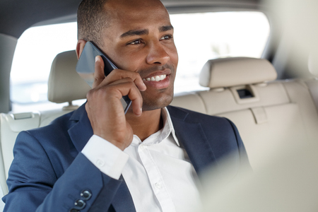 Young businessman sitting on back seat in car answering phone call smiling cheerful close-up side viewの写真素材