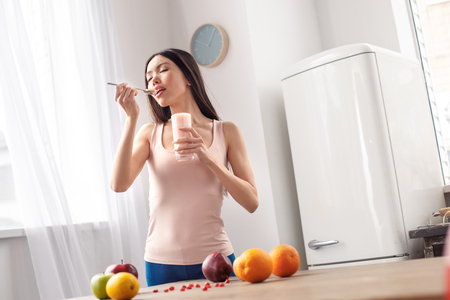Young girl at kitchen healthy lifestyle standing near window eating smoothie joyful tasty breakfastの写真素材