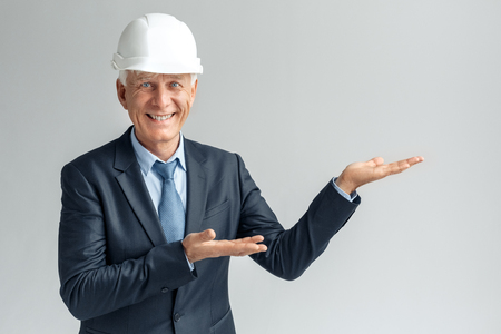 Professional Occupation. Constructor in hard hat standing isolated on gray showing space aside smiling happyの写真素材