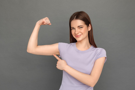 Freestyle. Young girl standing isolated on grey showing arm muscle smiling confident close-upの写真素材