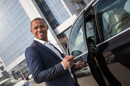 Young man standing opening car door with alarm key looking aside happyの写真素材
