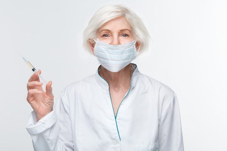 Senior woman doctor studio isolated on white wall holding syringe anti-aging injectionの写真素材