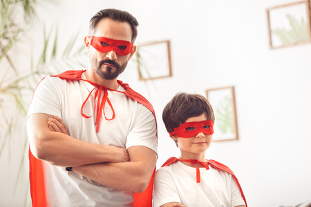 Father and son in superheroe costumes at home standing crossed arms looking camera seriousの写真素材