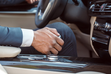 Young businessman driver sitting inside car holding gear shifter close-upの写真素材