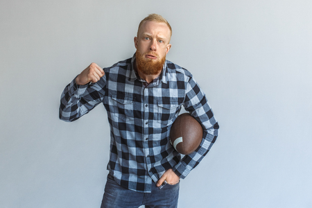 Freestyle. Mature man standing isolated on grey with ball showing fist agressiveの写真素材