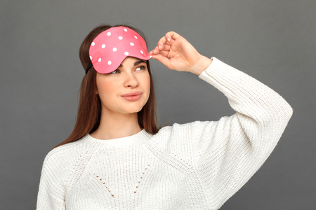 Freestyle. Young girl in sleeping mask standing isolated on grey smiling playful close-upの写真素材