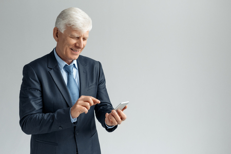 Business Lifestyle. Businessman standing isolated on gray browsing smartphone laughing joyfulの写真素材