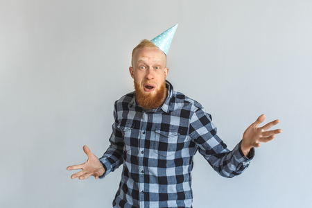 Birthday Concept. Mature man in cap standing isolated on grey hands aside looking camera surprisedの写真素材